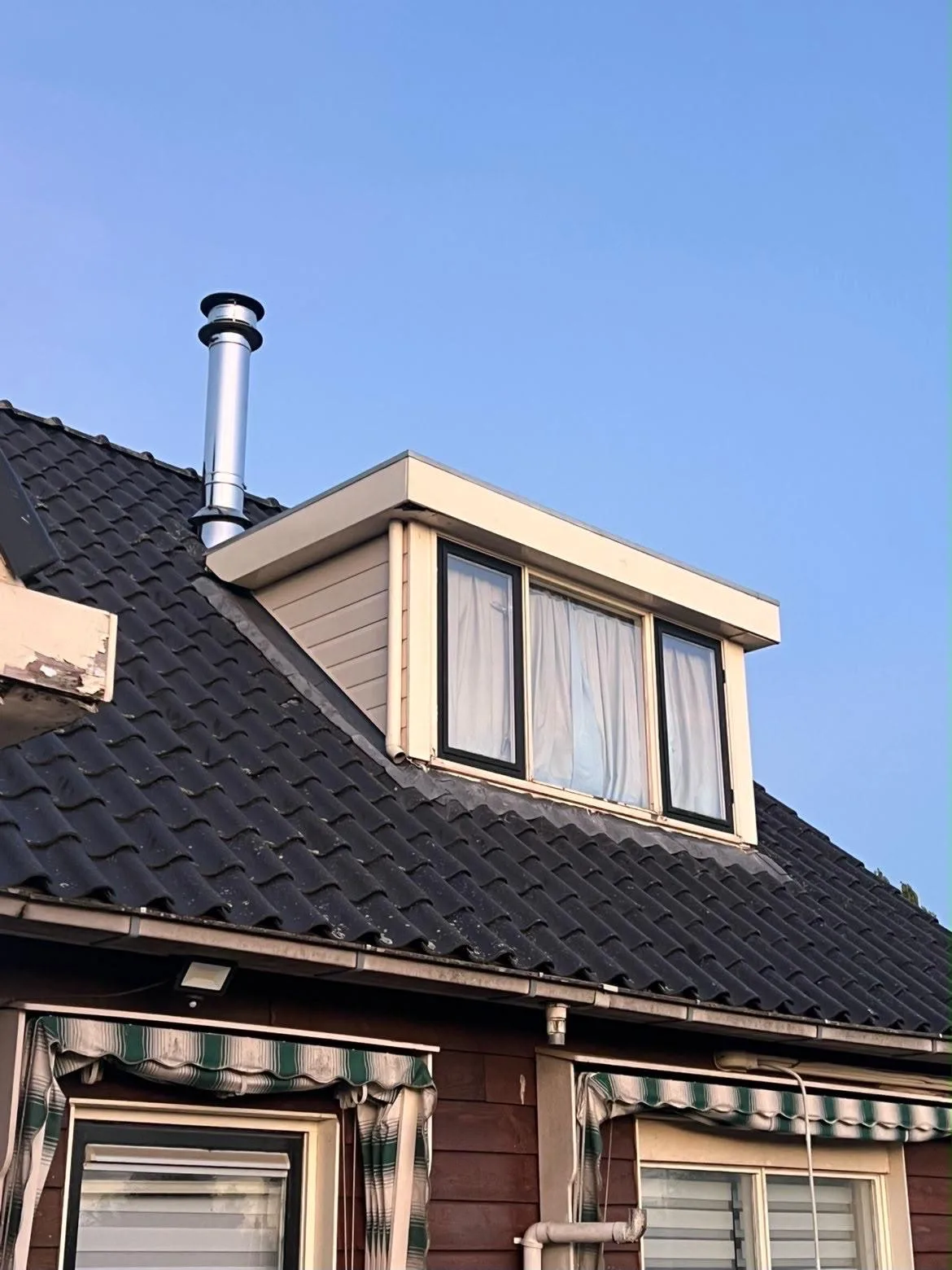 Witte dakkapel op een donker pannendak na de reiniging