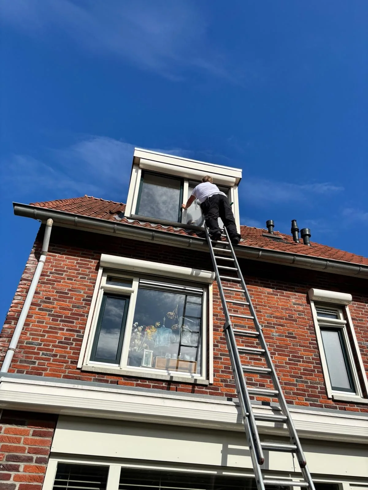 Glazenwasser van AS Cleaning op de ladder bij een dakkapel